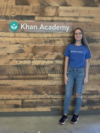 Khan Academy'nin mavi tişörtünü giyen Lara, Khan Academy tabelası önünde poz veriyor