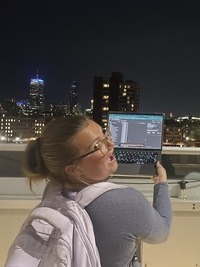 An image of Anastasia wearing a purple sweater, holding up laptop against the Boston skyline.