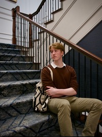 Carter sitting posed on some stairs, wearing a burgandy sweater over a white collared shirt