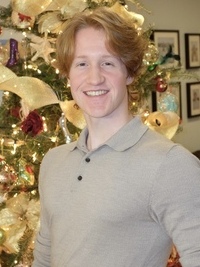 A headshot of Carter wearing a beige collared shirt in front of a Christmas tree