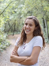 Hannah smiling in a forest with arms crossed.
