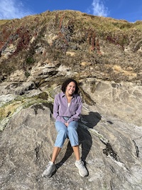 Madeleine, kumsaldaki bir kayanın üzerinde oturuyor.