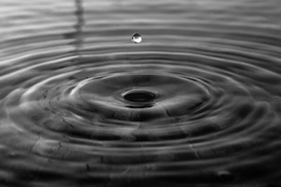 Water drips fall on a surface of water, creating circular waves that spread outward