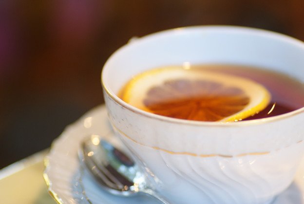A cup of black tea with a slice of lemon in a white teacup with a saucer. 