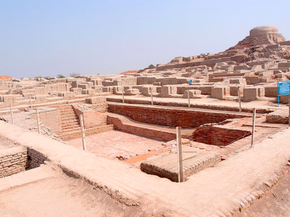 The Great Bath at Mohenjo-daro: Amid the brick ruins of a 3rd-millennium BCE city, stairs descend on two sides into a large, rectangular brick-lined pit.  Wooden stakes and wire encircle the perimeter, preventing entry by modern-day tourists.