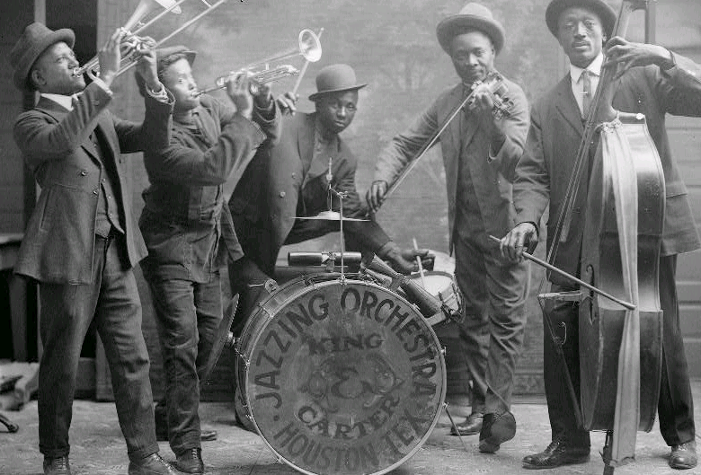 Photograph of a jazz quintet. African American men play horns, drums, and string instruments. 