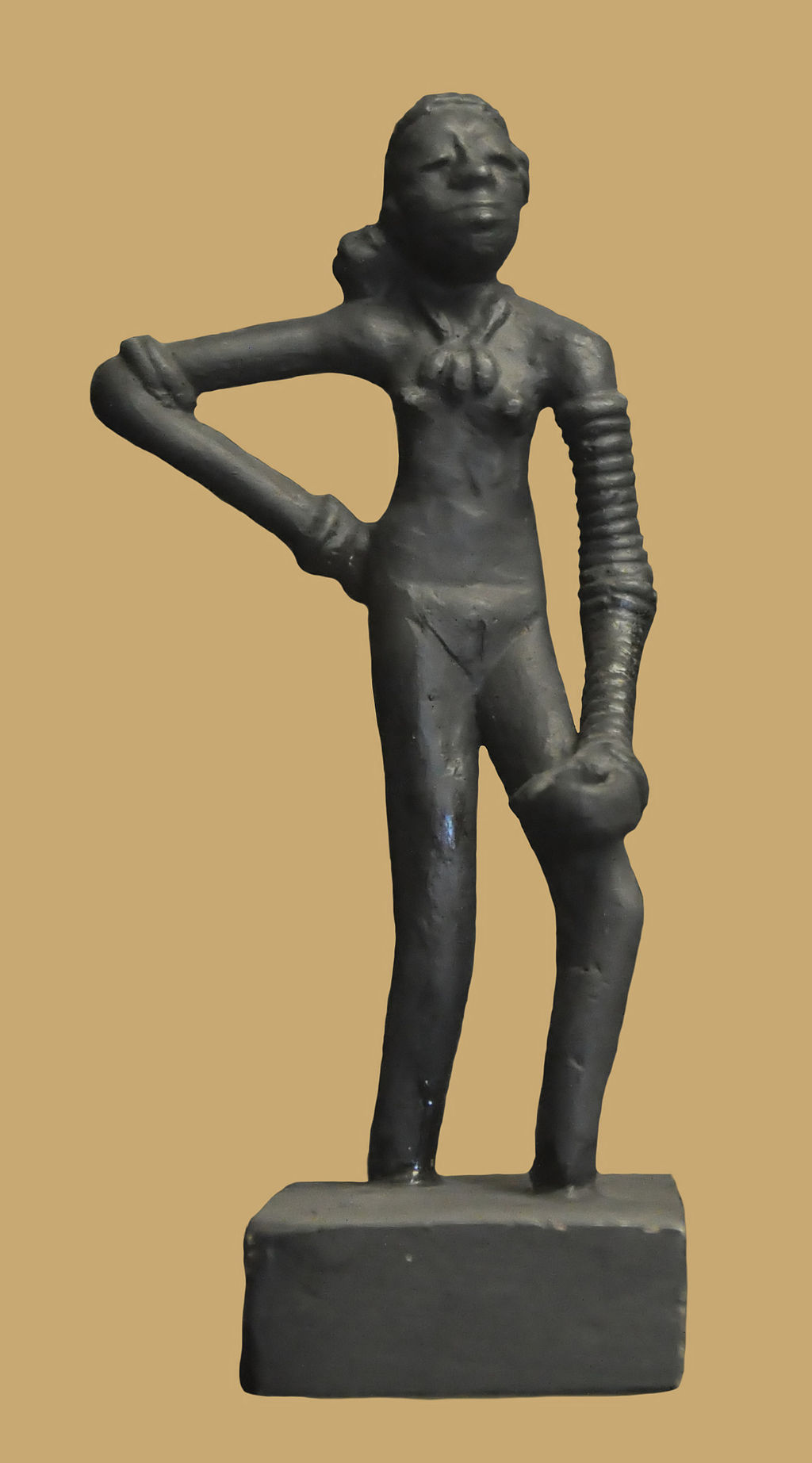 Bronze figurine of a woman posed with her right hand on her hip. She wears a necklace and her left arm is bound with something, possibly jewelry or rope. 