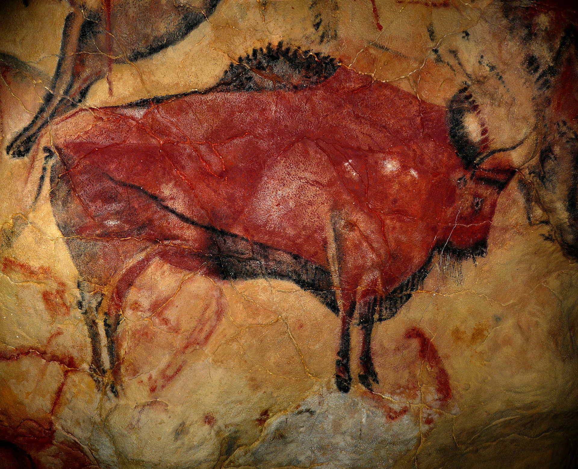 A bison figure painted with red pigment on a smooth tan-colored surface with some visible cracks. The painter also utilized black strokes to add detail. 