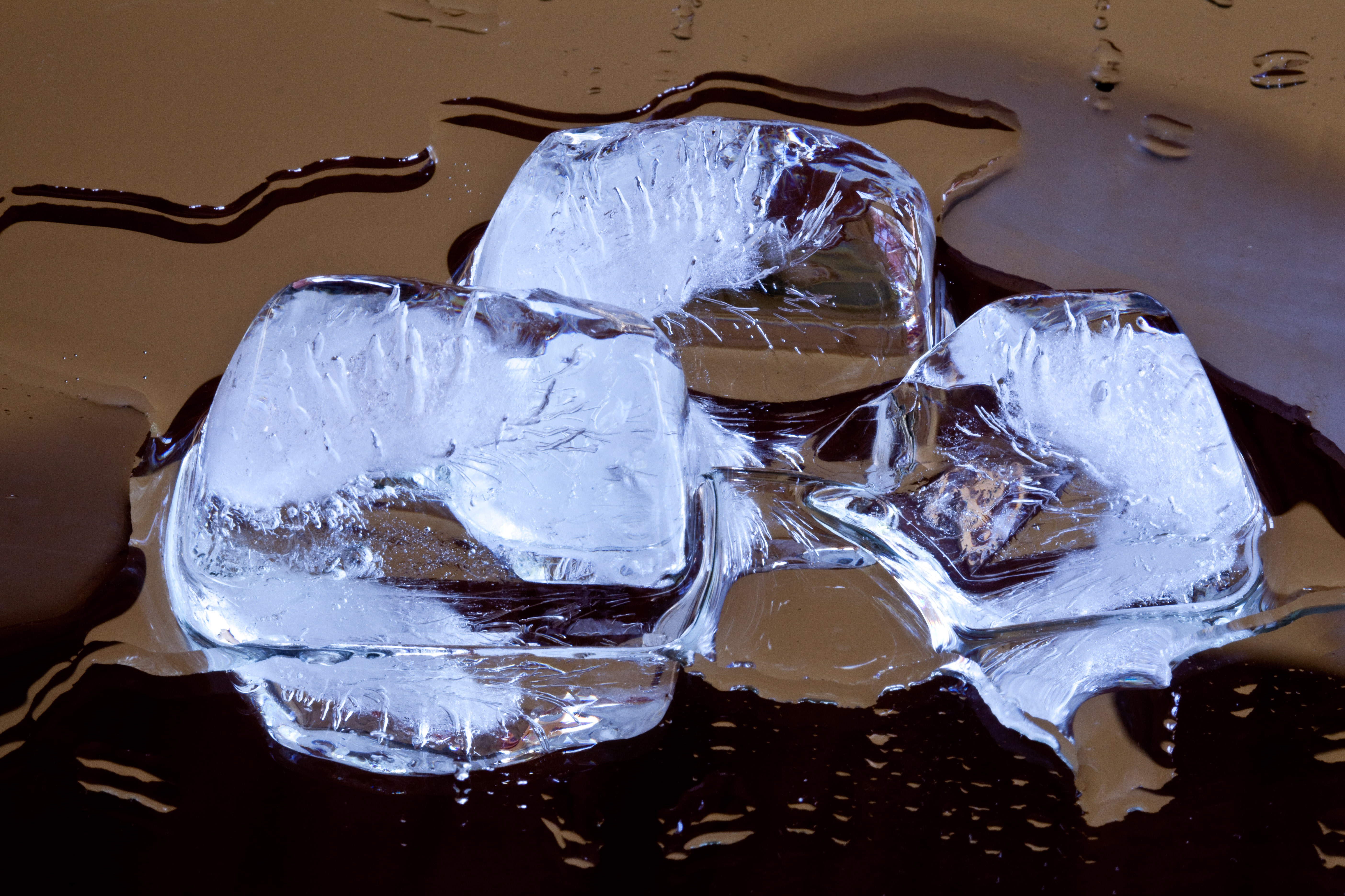 Three melting ice cubes in a puddle of water on a mirrored surface.